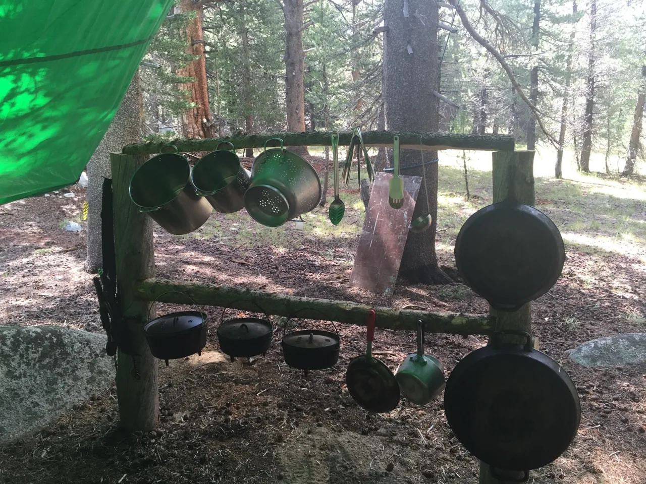 Cooking pots, utensils, and cast-iron pans hanging from a wooden camp rack