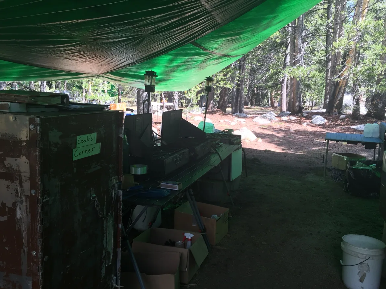 Stoves and work surfaces arranged beneath a green tarp in a forest field kitchen