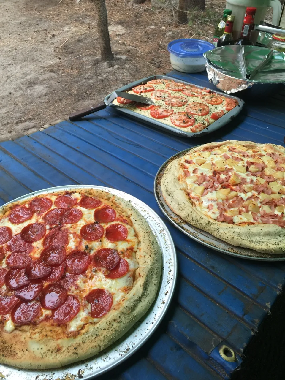 Finished pizzas and a baked tomato dish arranged on a camp worktable