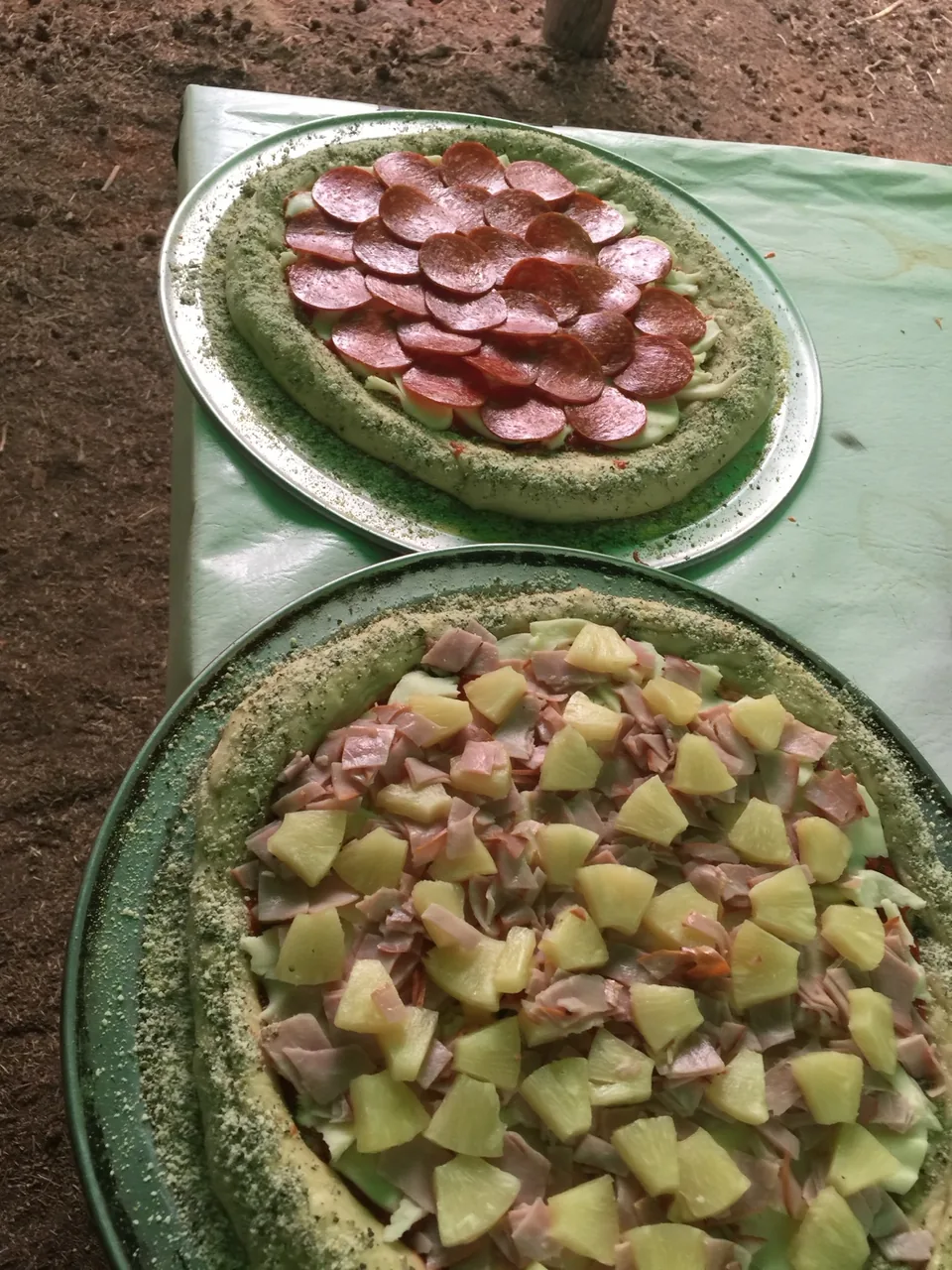 Two fully topped uncooked pizzas prepared on an outdoor worktable