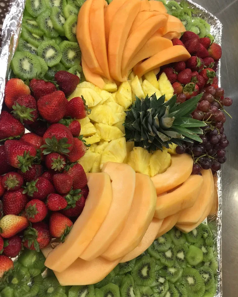 A large fruit platter arranged with kiwi, cantaloupe, strawberries, pineapple, and grapes