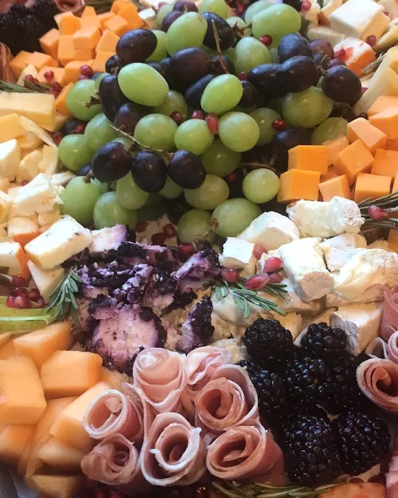 A grazing board arranged with grapes, cheeses, rolled cured meats, blackberries, and herbs
