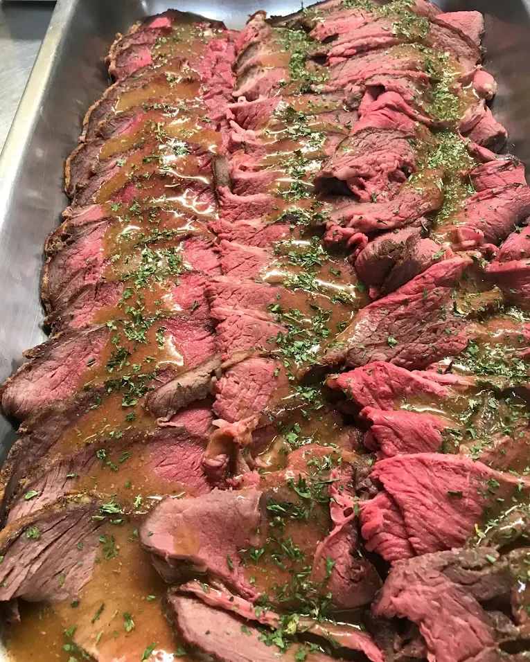 Sliced pink-centered beef with sauce and herbs in a metal service pan