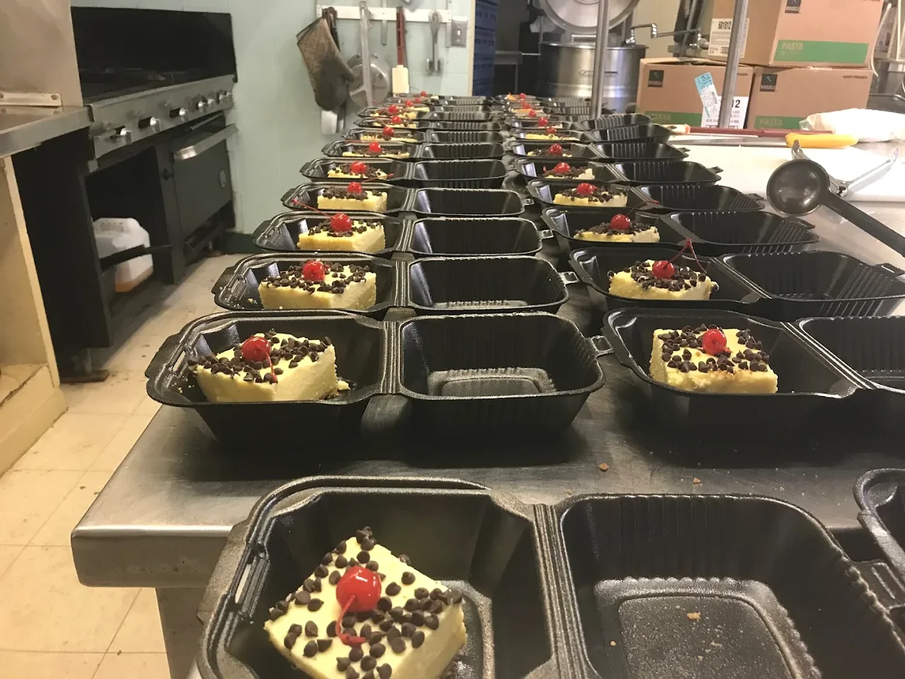 Rows of black divided containers with individual dessert portions on a commercial-kitchen worktable