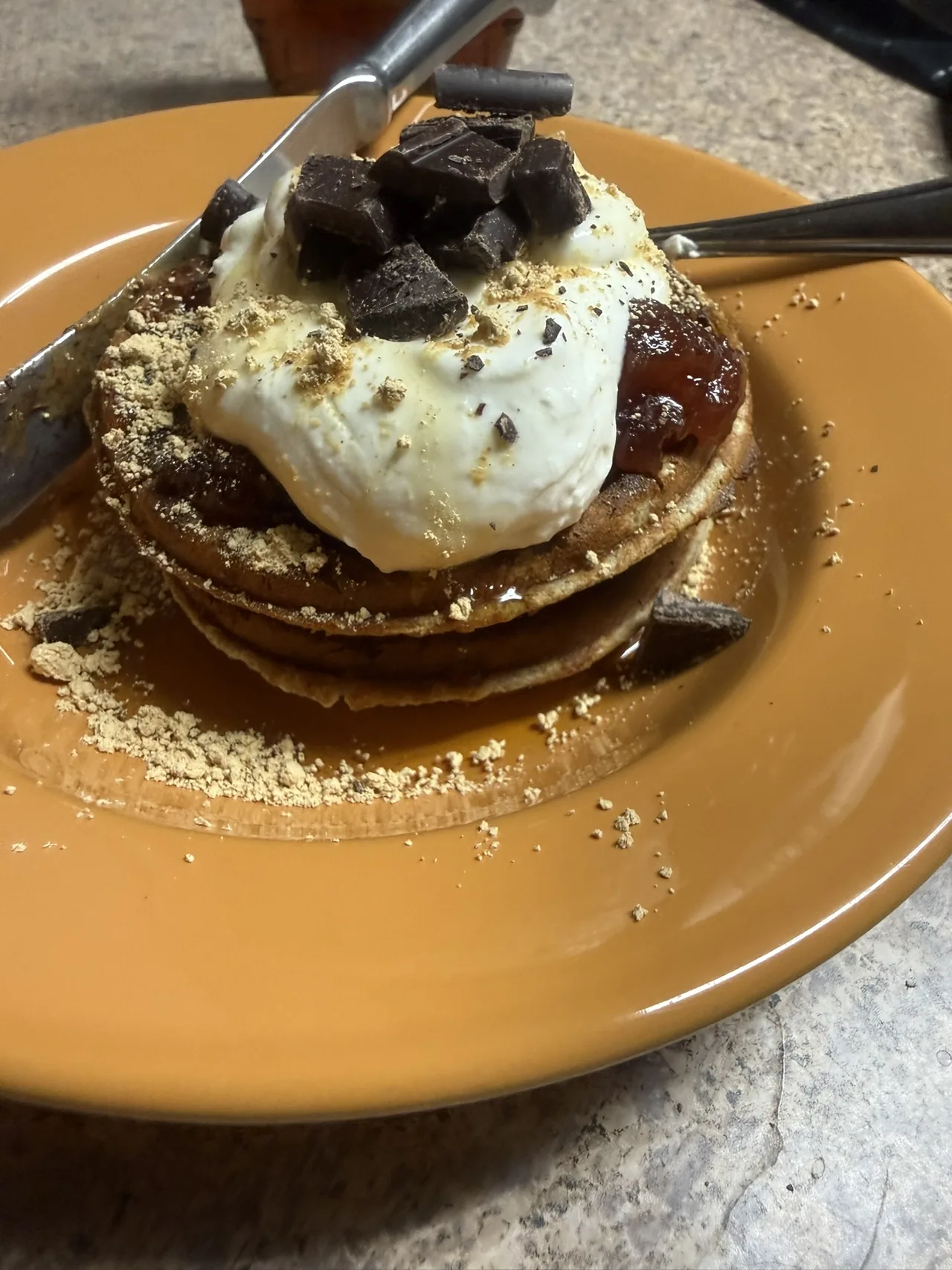 Pancakes topped with cream, fruit preserve, chocolate, and crumble