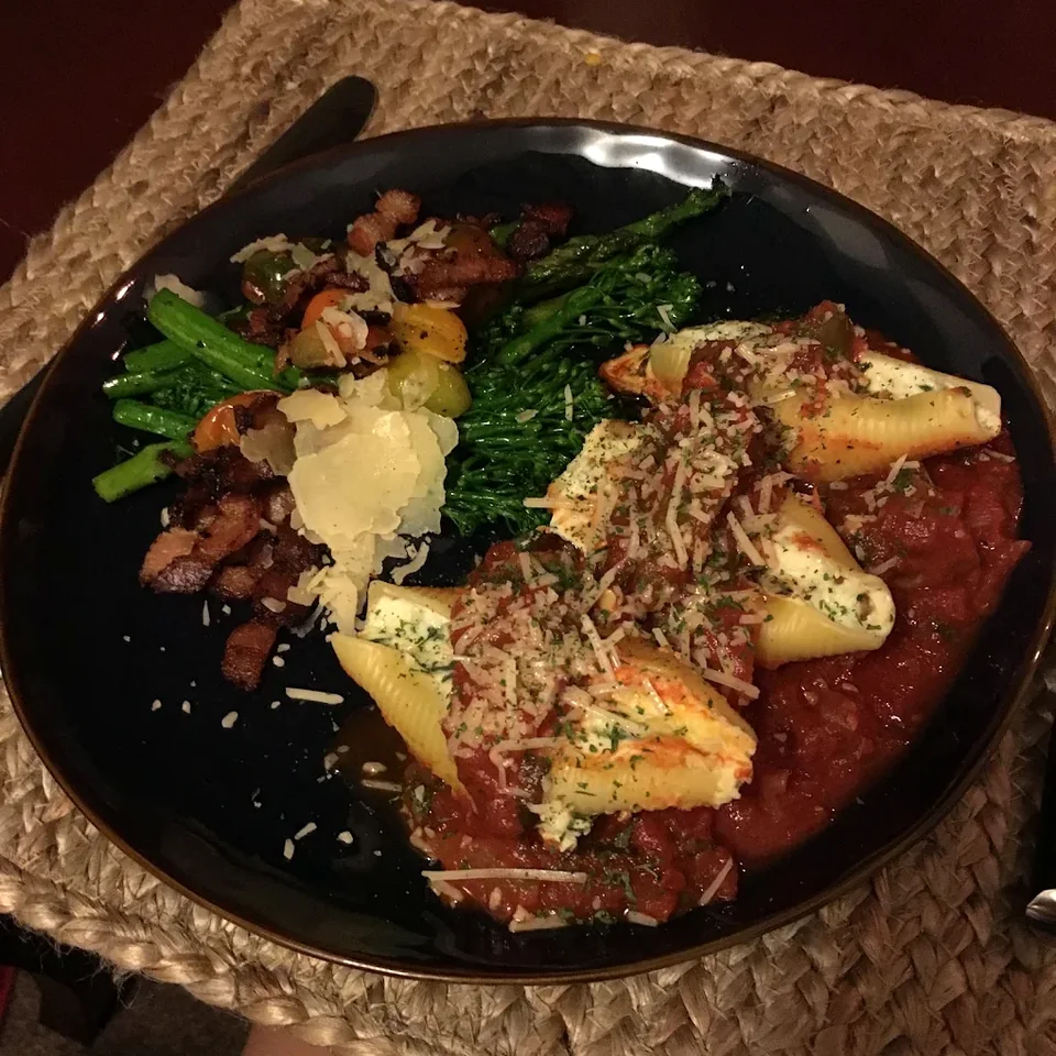 Stuffed pasta shells with tomato sauce and green vegetables on a black plate